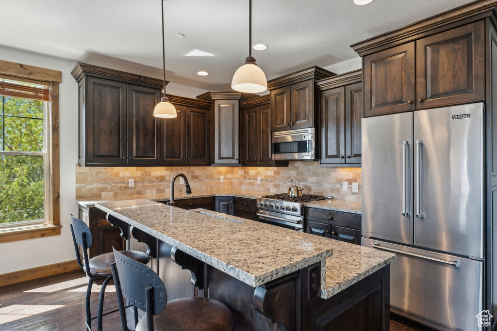 Kitchen featuring dark brown cabinetry, dark wood-style floors, high quality appliances, light stone counters, and a sink