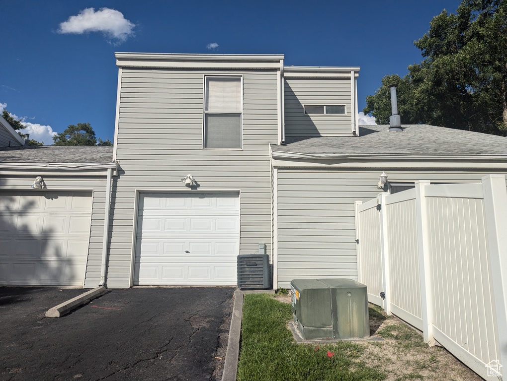 Garage with central AC unit, aphalt driveway, and fence