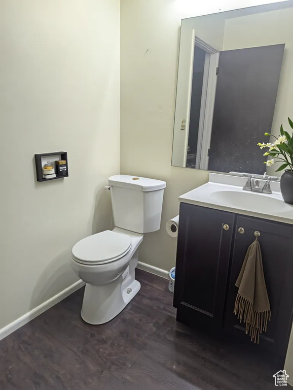 Half bathroom with toilet, wood finished floors, baseboards, and vanity