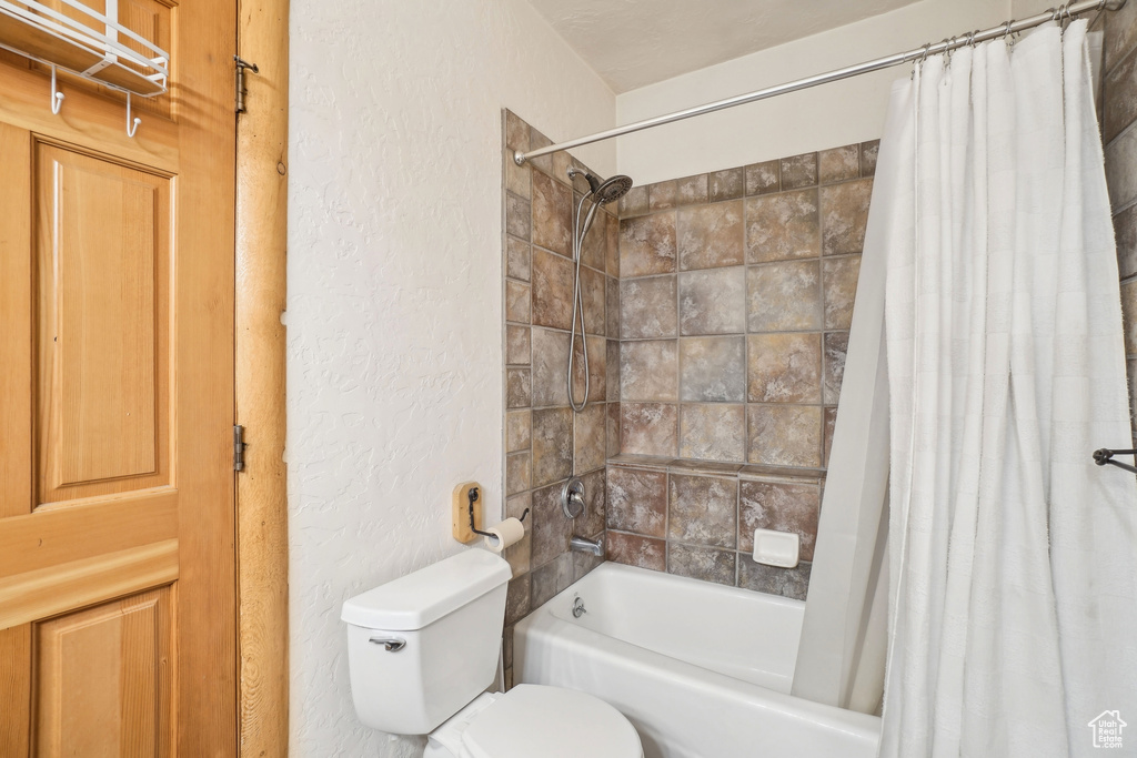 Full bathroom with toilet, a textured wall, and shower / bath combo with shower curtain