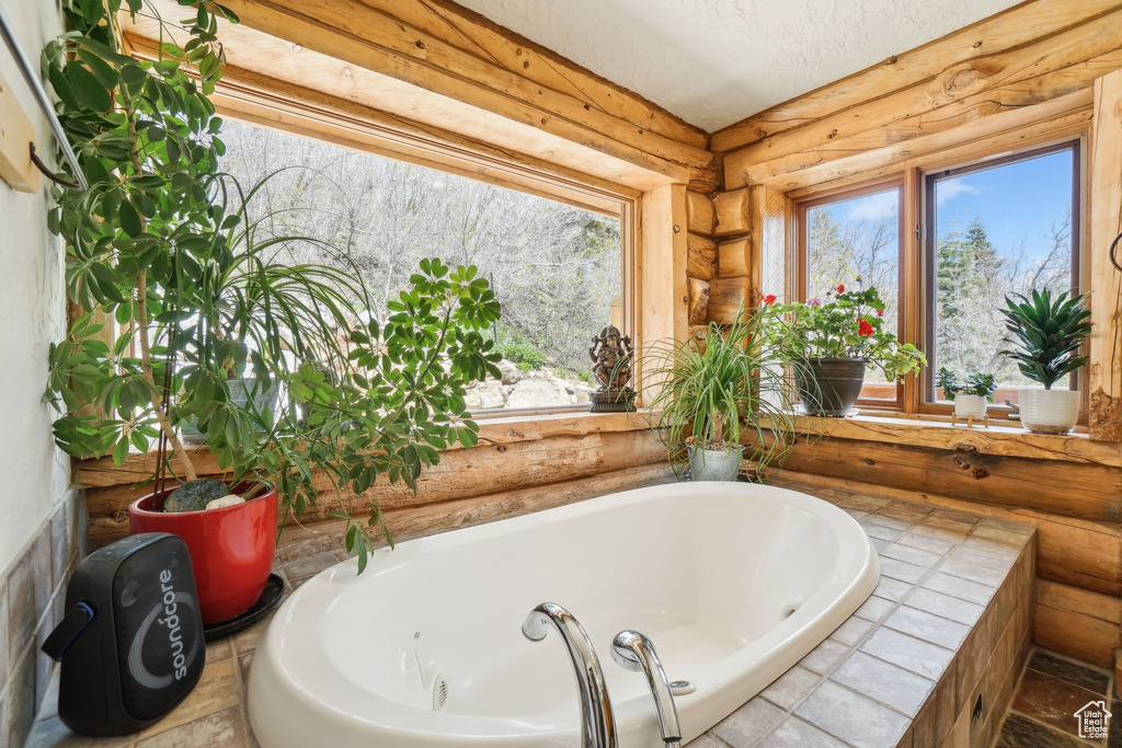 Full bath featuring a garden tub, plenty of natural light, and log walls