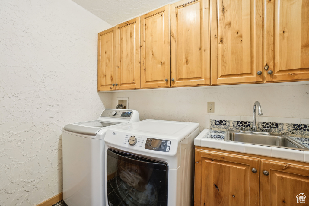 Clothes washing area with cabinet space, washer and clothes dryer, a sink, and a textured wall