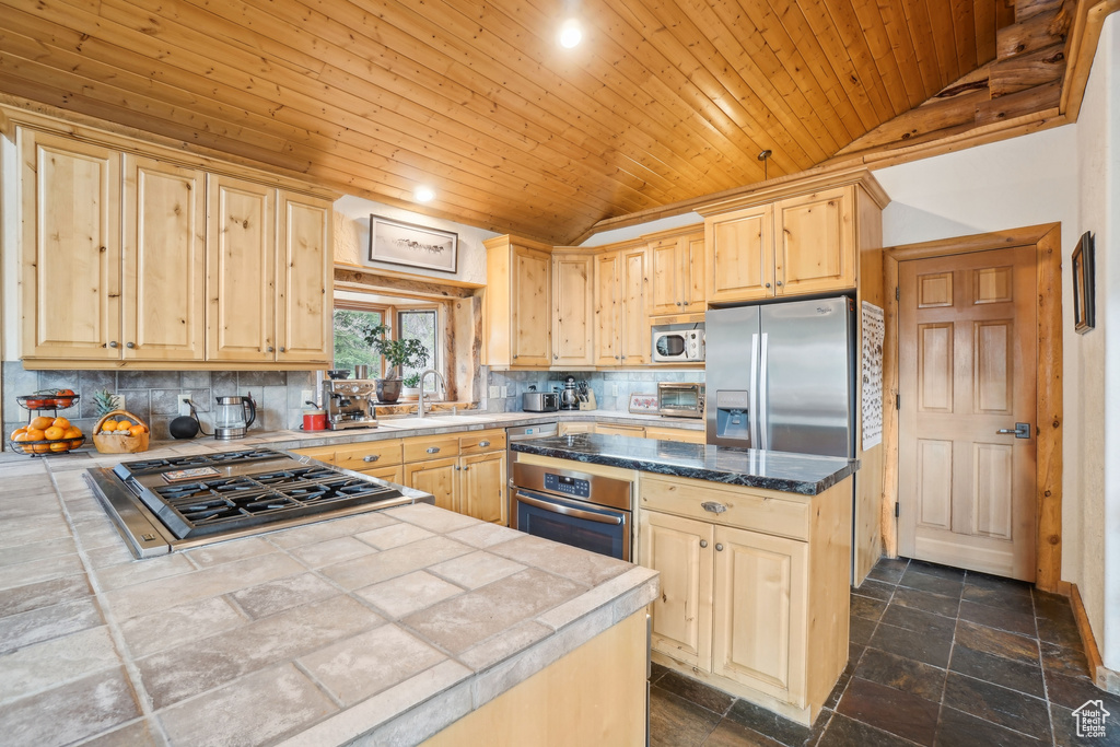 Kitchen with lofted ceiling, wooden ceiling, stone tile floors, light brown cabinetry, and appliances with stainless steel finishes