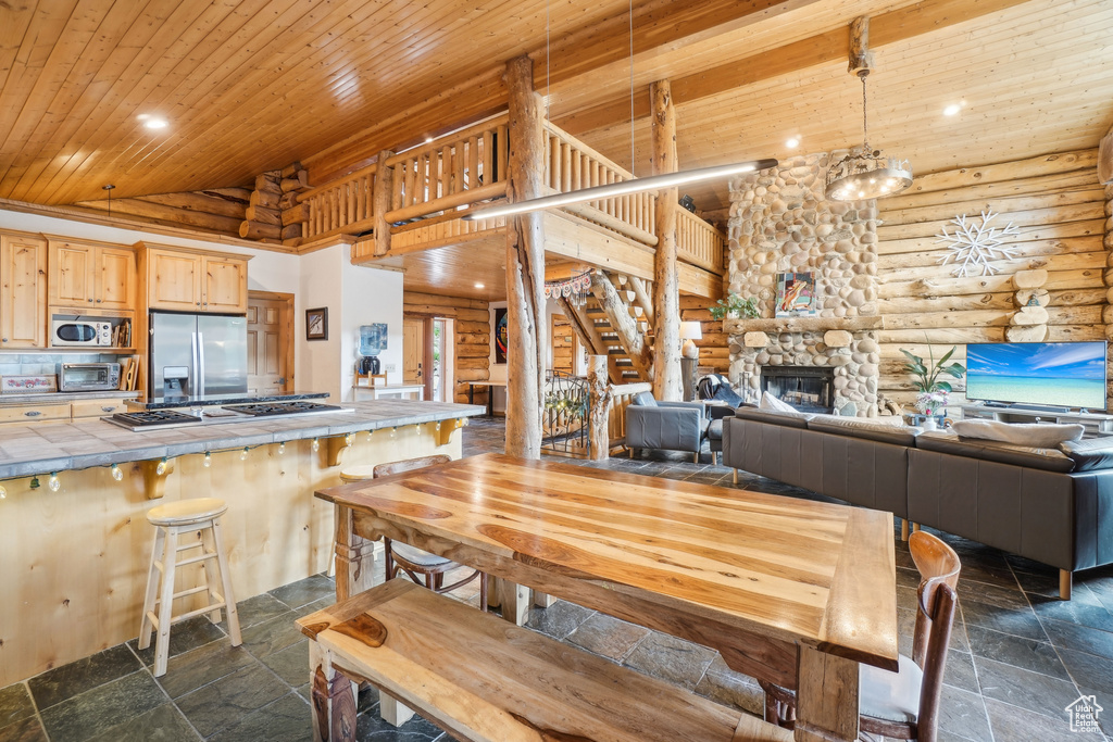 Dining room featuring log walls, stone tile floors, wood ceiling, and high vaulted ceiling