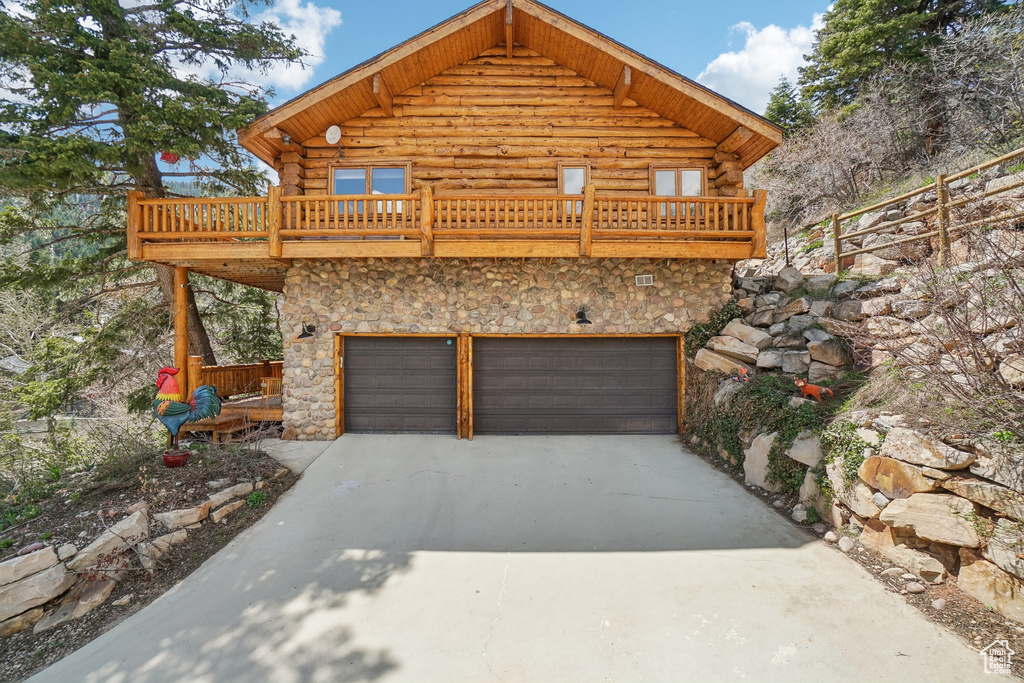 View of front of property with stone siding, concrete driveway, log exterior, and a garage