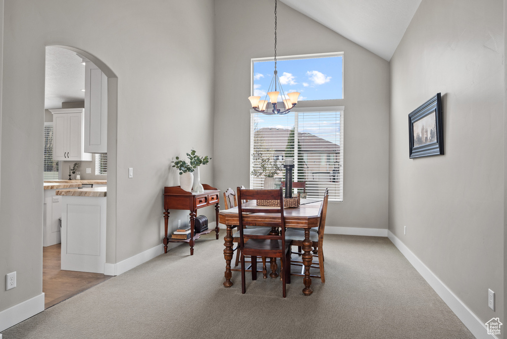 Dining area with baseboards, a chandelier, high vaulted ceiling, arched walkways, and light carpet