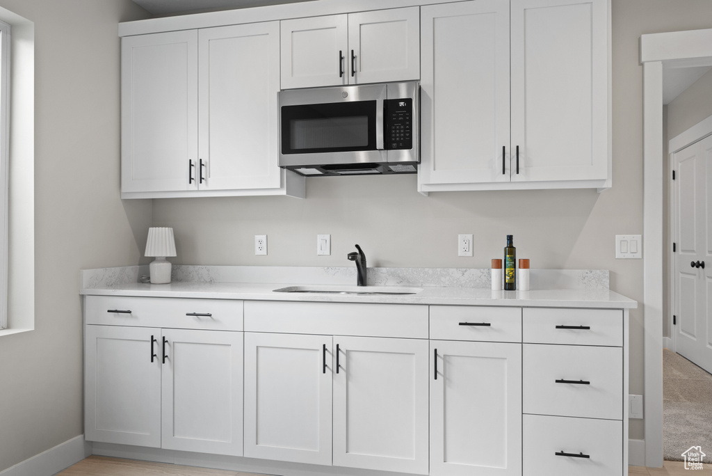 Kitchen with stainless steel microwave, white cabinetry, a sink, and light countertops