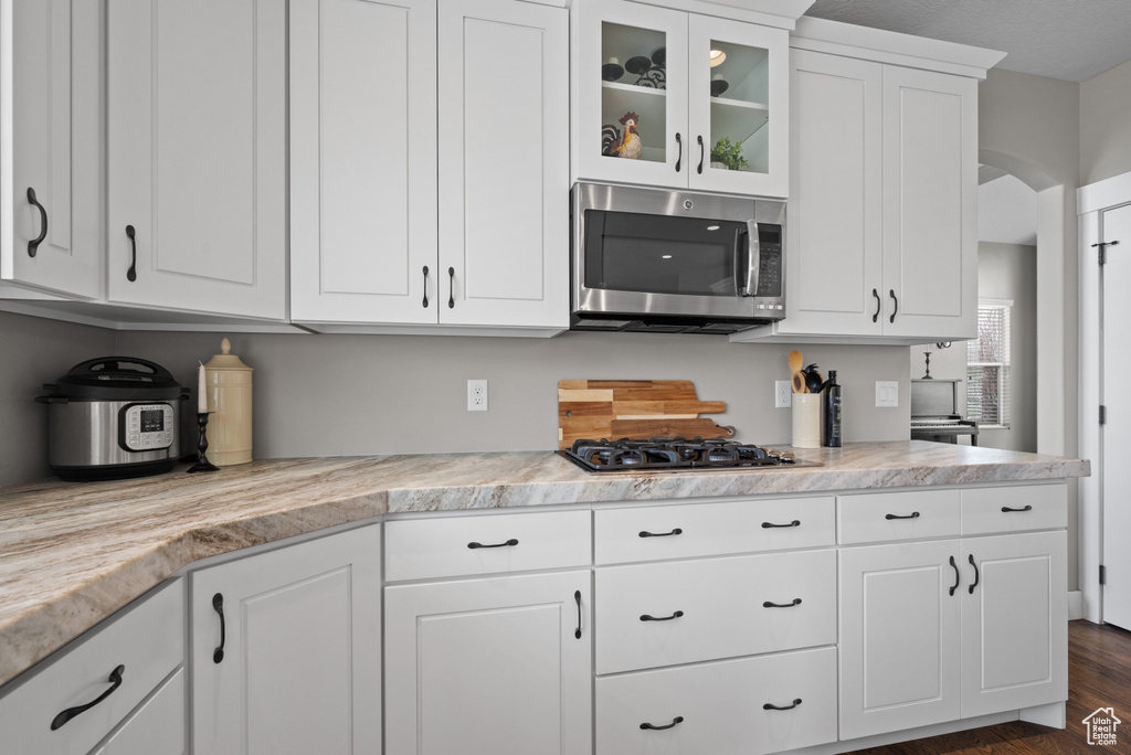 Kitchen with arched walkways, light countertops, glass insert cabinets, white cabinets, and appliances with stainless steel finishes