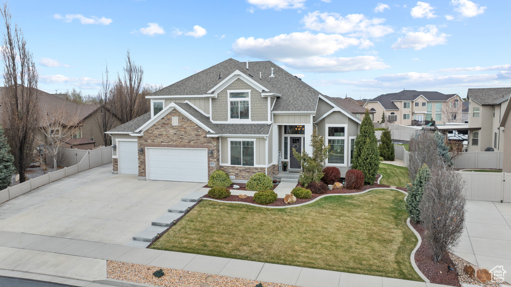 View of front of home featuring concrete driveway, stone siding, a shingled roof, and fence