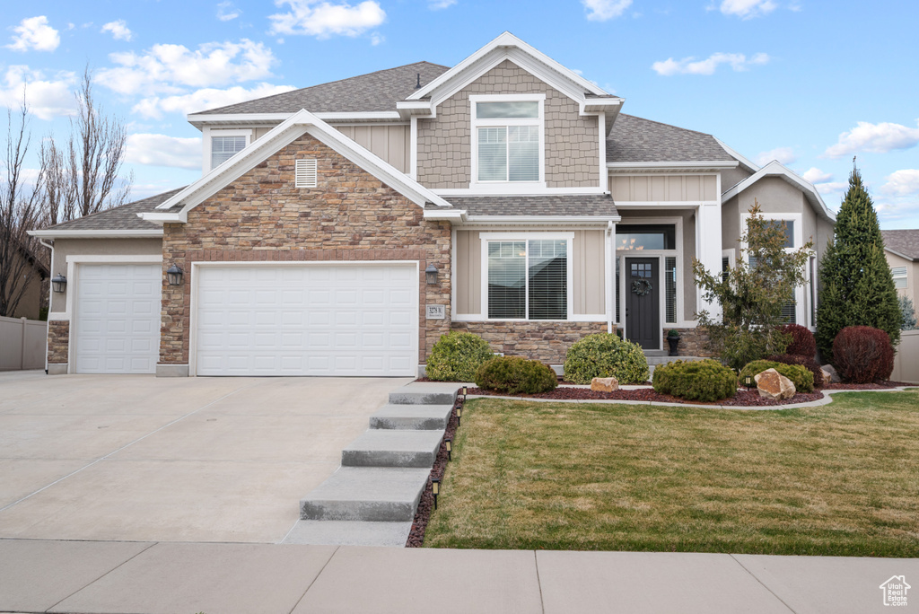 Craftsman-style house featuring board and batten siding, a front yard, a garage, concrete driveway, and stone siding