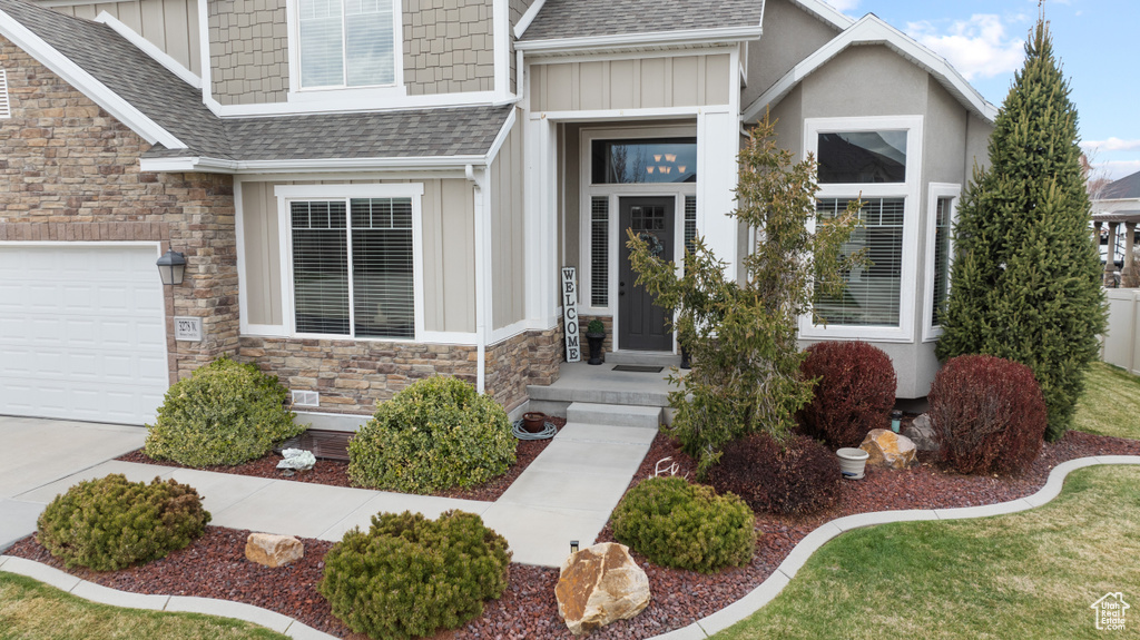 Entrance to property with roof with shingles, stone siding, and board and batten siding