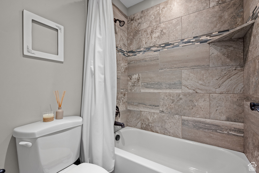 Bathroom featuring toilet and shower / bathtub combination with curtain
