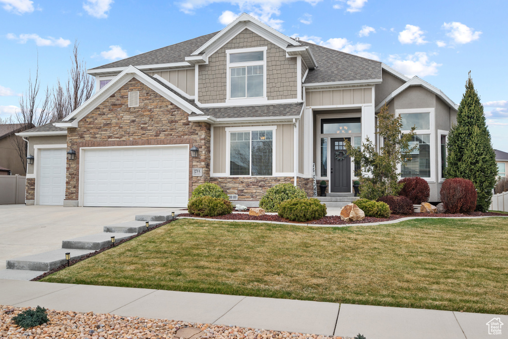Craftsman inspired home featuring stone siding, driveway, a garage, a front lawn, and board and batten siding