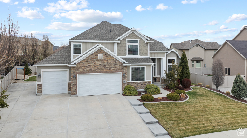 Craftsman house featuring roof with shingles, fence, stone siding, concrete driveway, and a front lawn
