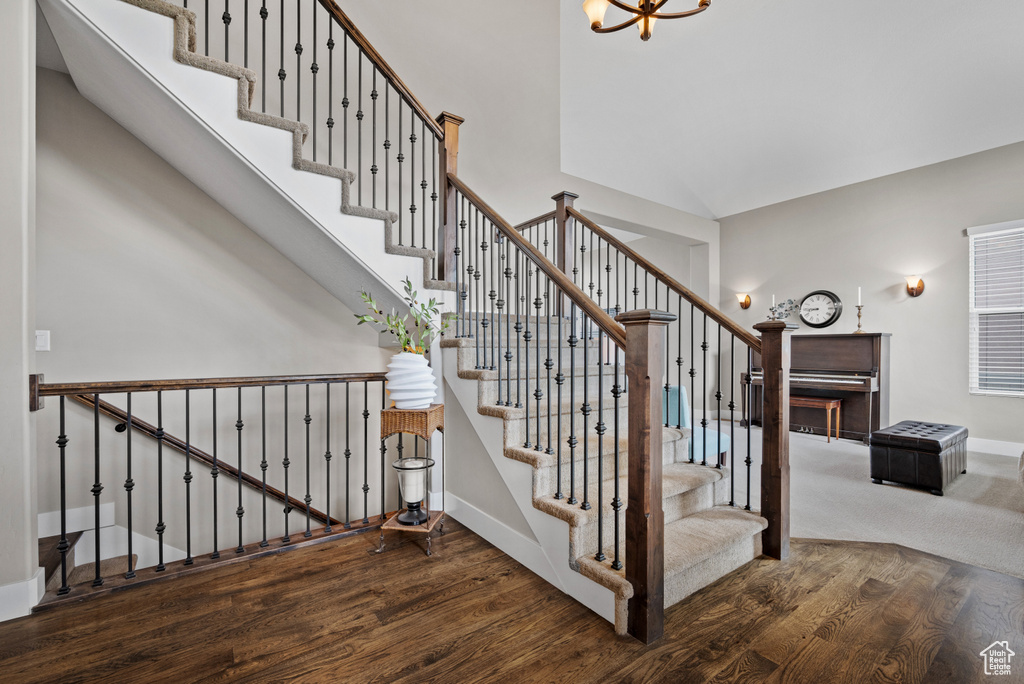 Stairs featuring a high ceiling, baseboards, a notable chandelier, and wood finished floors