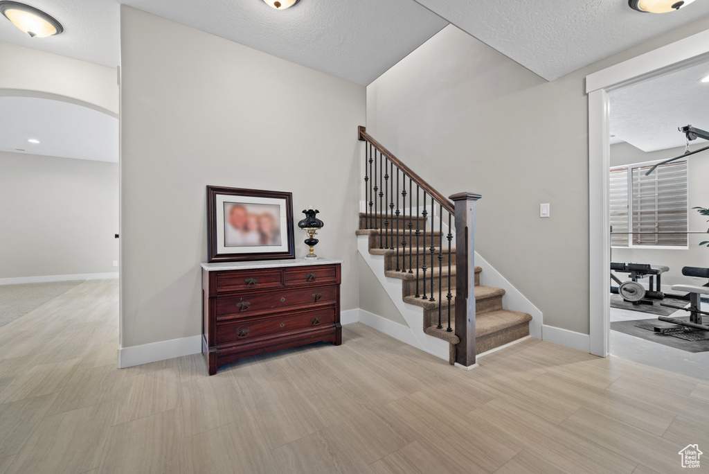 Staircase featuring a textured ceiling, arched walkways, baseboards, and wood finished floors