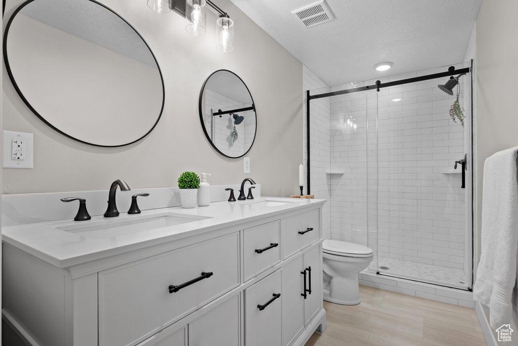 Bathroom featuring double vanity, toilet, a stall shower, and a sink