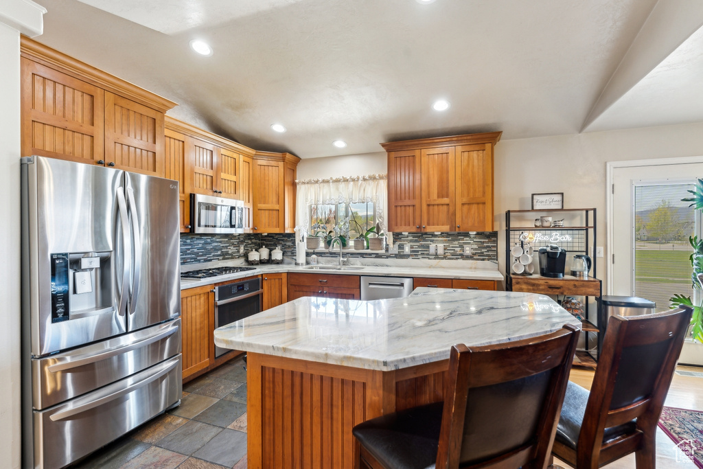 Kitchen featuring stainless steel appliances, decorative backsplash, recessed lighting, a sink, and dark stone finish flooring