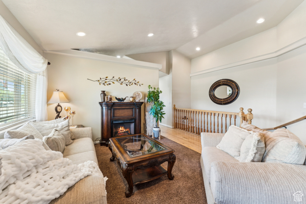 Living room with recessed lighting, lofted ceiling, a glass covered fireplace, wood finished floors, and baseboards