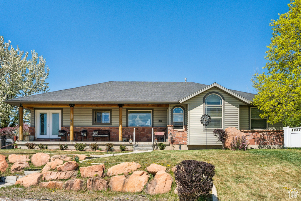 Single story home with a porch, a front lawn, french doors, and roof with shingles