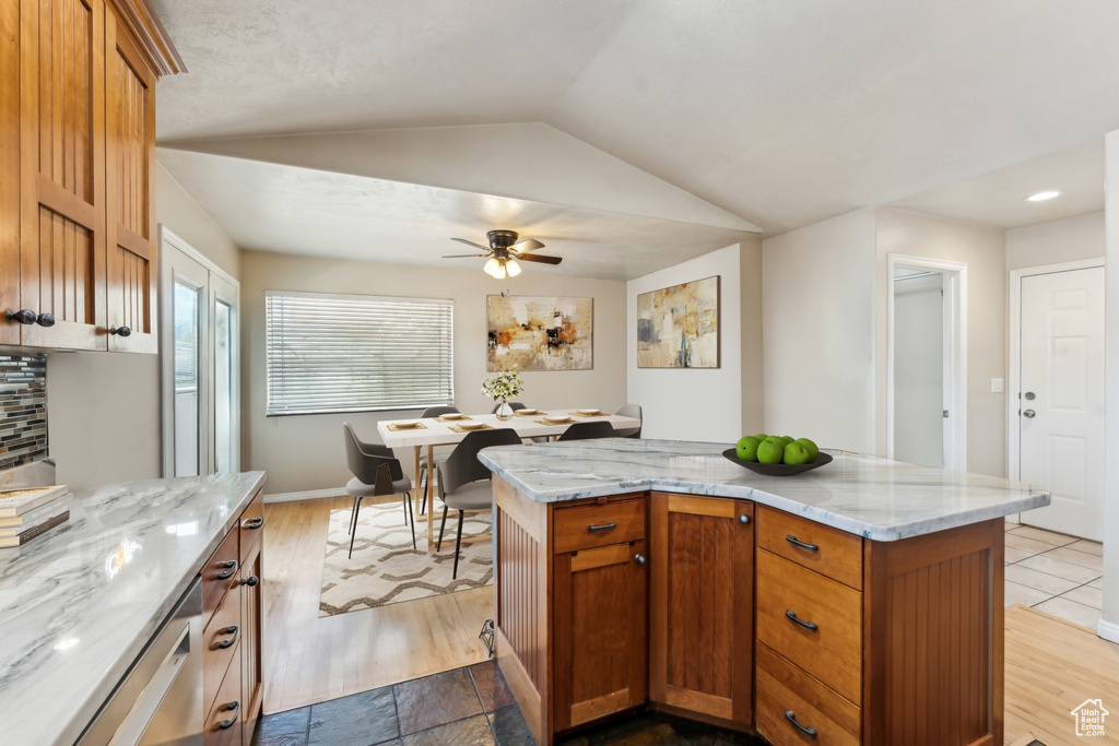 Kitchen with ceiling fan, light stone countertops, vaulted ceiling, a kitchen island, and brown cabinetry
