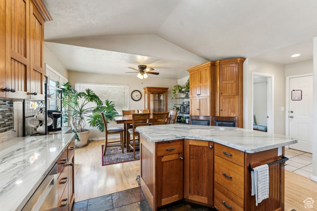 Kitchen with a ceiling fan, lofted ceiling, light stone counters, a kitchen island, and decorative backsplash
