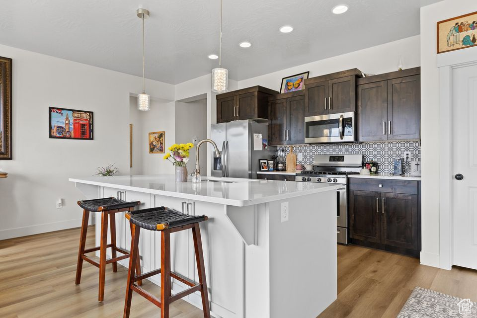 Kitchen featuring stainless steel appliances, a sink, decorative backsplash, a kitchen bar, and light wood-style floors