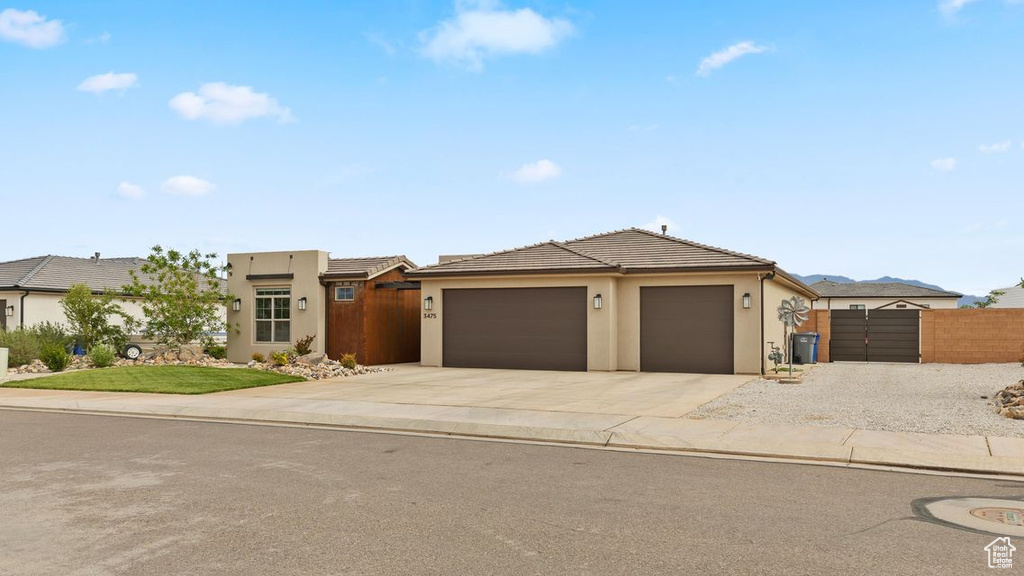 View of front of home featuring stucco siding, driveway, an attached garage, a gate, and fence
