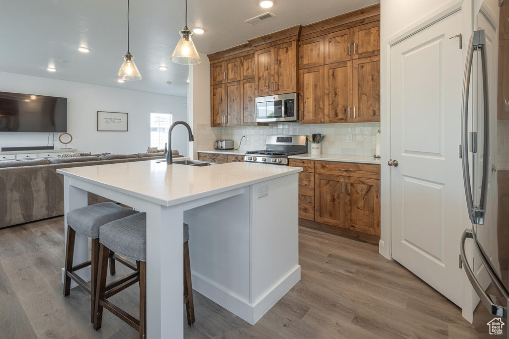Kitchen with a breakfast bar area, brown cabinetry, open floor plan, stainless steel appliances, and tasteful backsplash