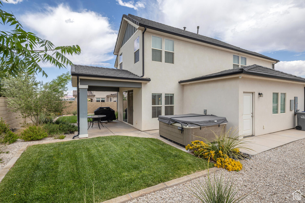 Back of property with stucco siding, a lawn, a hot tub, a fenced backyard, and a patio area
