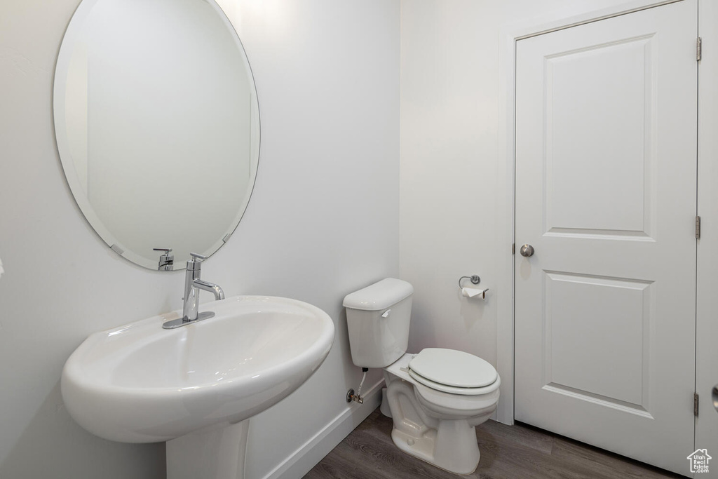 Bathroom featuring toilet, wood finished floors, baseboards, and a sink