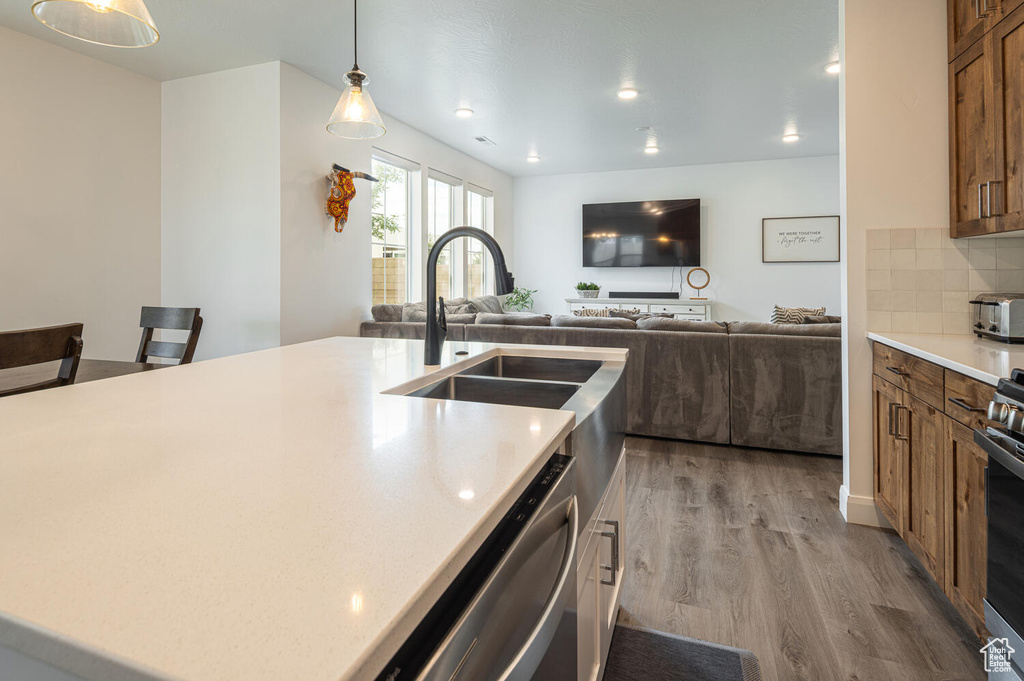 Kitchen featuring a sink, brown cabinetry, open floor plan, light wood-type flooring, and stainless steel dishwasher