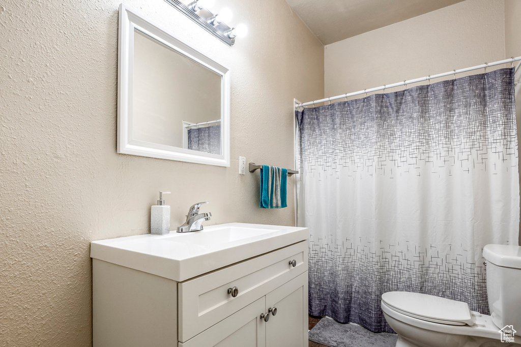 Full bath with vanity, toilet, and a textured wall