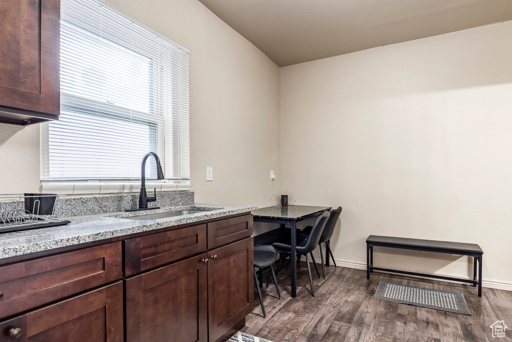 Kitchen with dark brown cabinetry, light stone counters, wood finished floors, and a sink