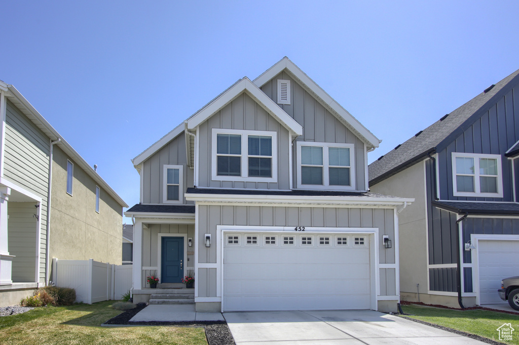 View of front of home with board and batten siding, fence, an attached garage, and driveway
