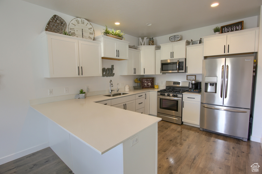 Kitchen with wood finished floors, a sink, light countertops, white cabinets, and stainless steel appliances