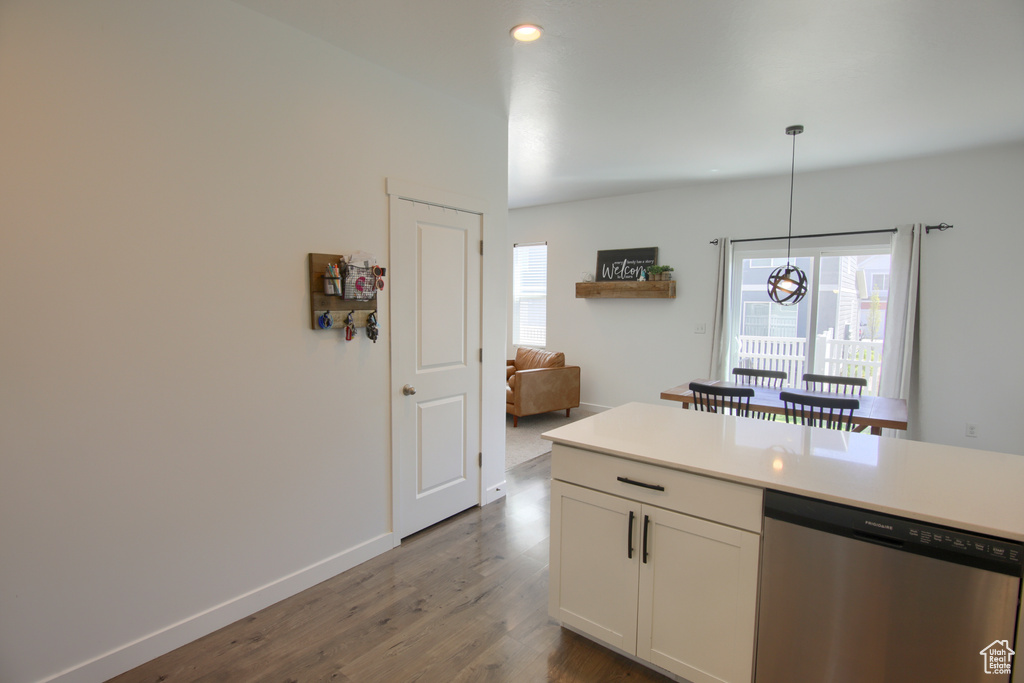 Kitchen featuring stainless steel dishwasher, dark wood-style floors, light countertops, white cabinets, and decorative light fixtures