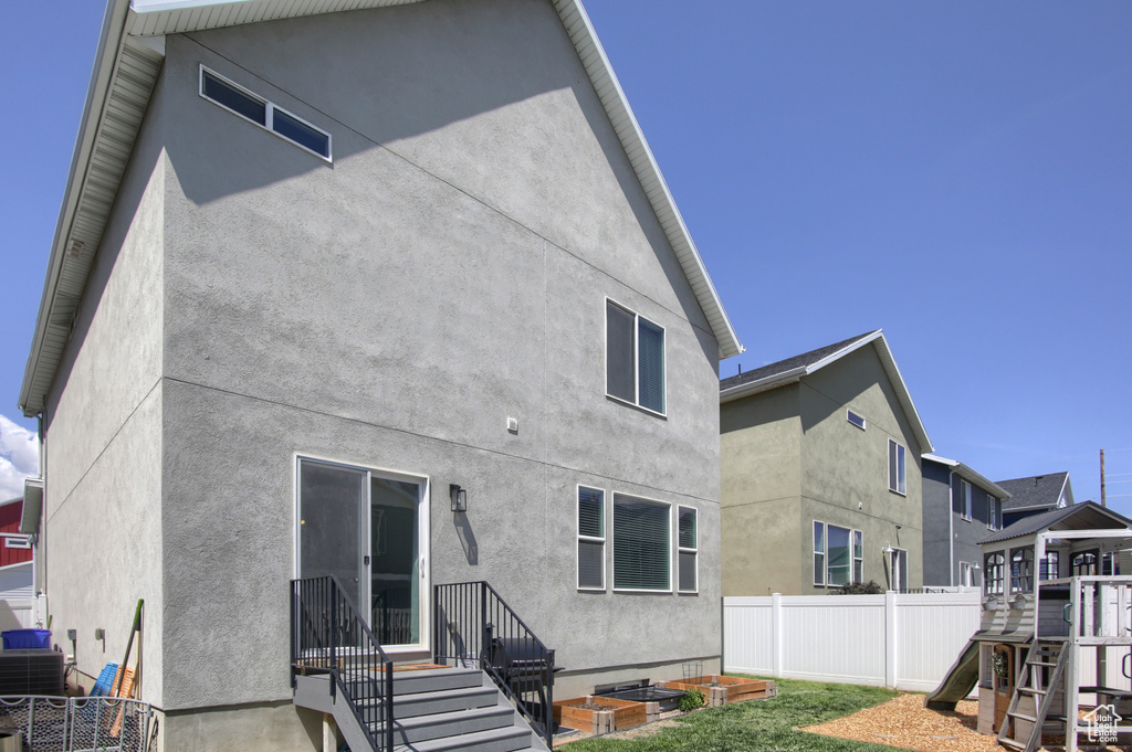 Rear view of property with fence, stucco siding, a playground, and central AC