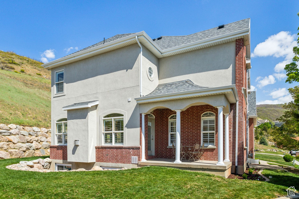 View of front of home featuring a shingled roof, a front lawn, brick siding, stucco siding, and covered porch