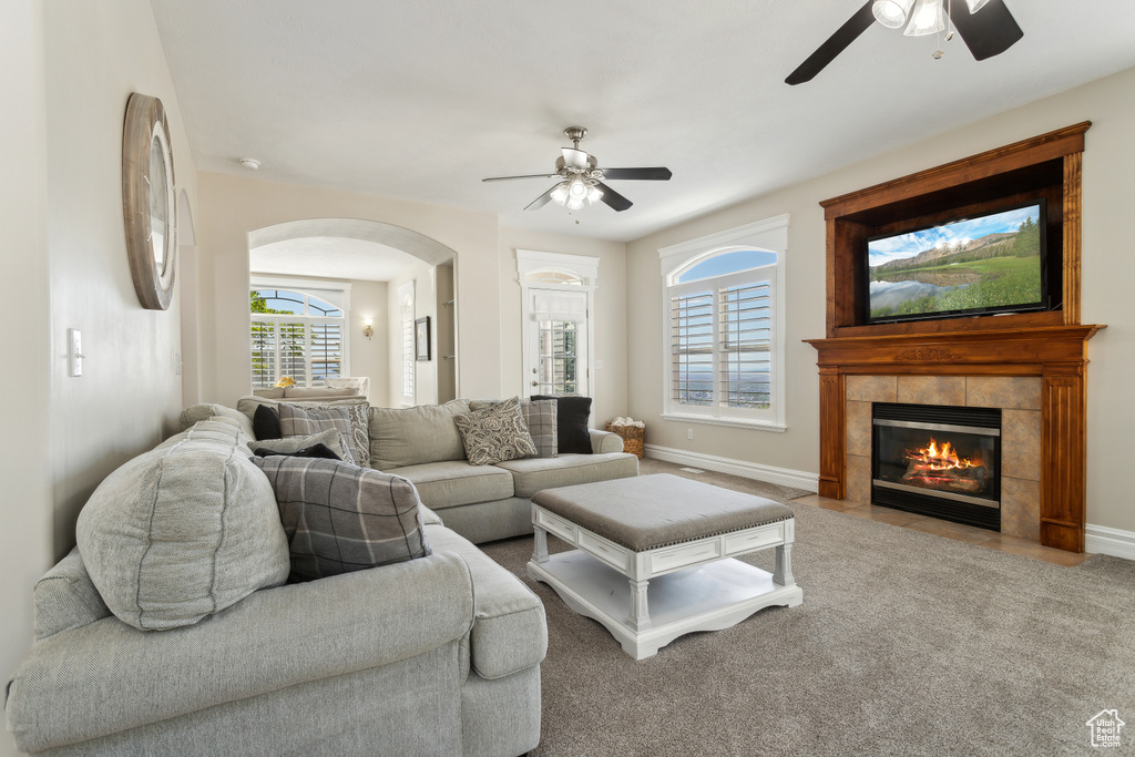 Living room with carpet flooring, baseboards, arched walkways, a tiled fireplace, and a ceiling fan
