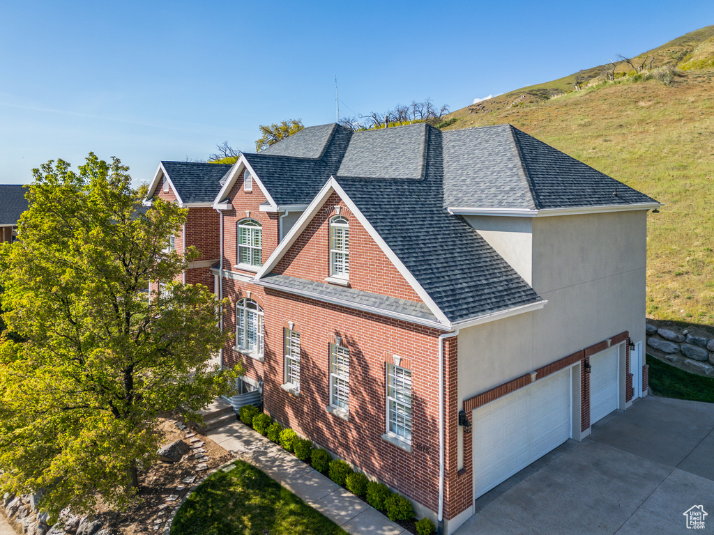 View of side of property with concrete driveway, brick siding, a shingled roof, and a garage