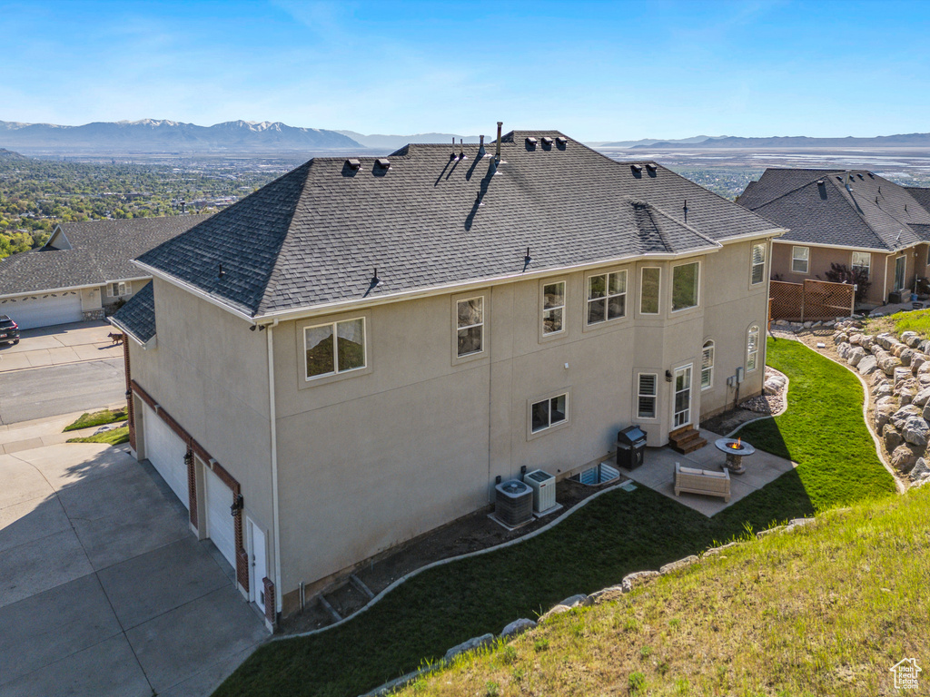 Back of house with a lawn, a shingled roof, a mountain view, and stucco siding