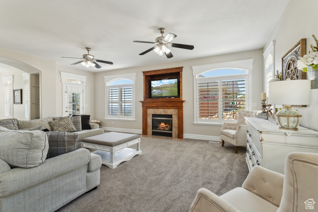 Carpeted living area featuring a tiled fireplace, arched walkways, baseboards, and a ceiling fan