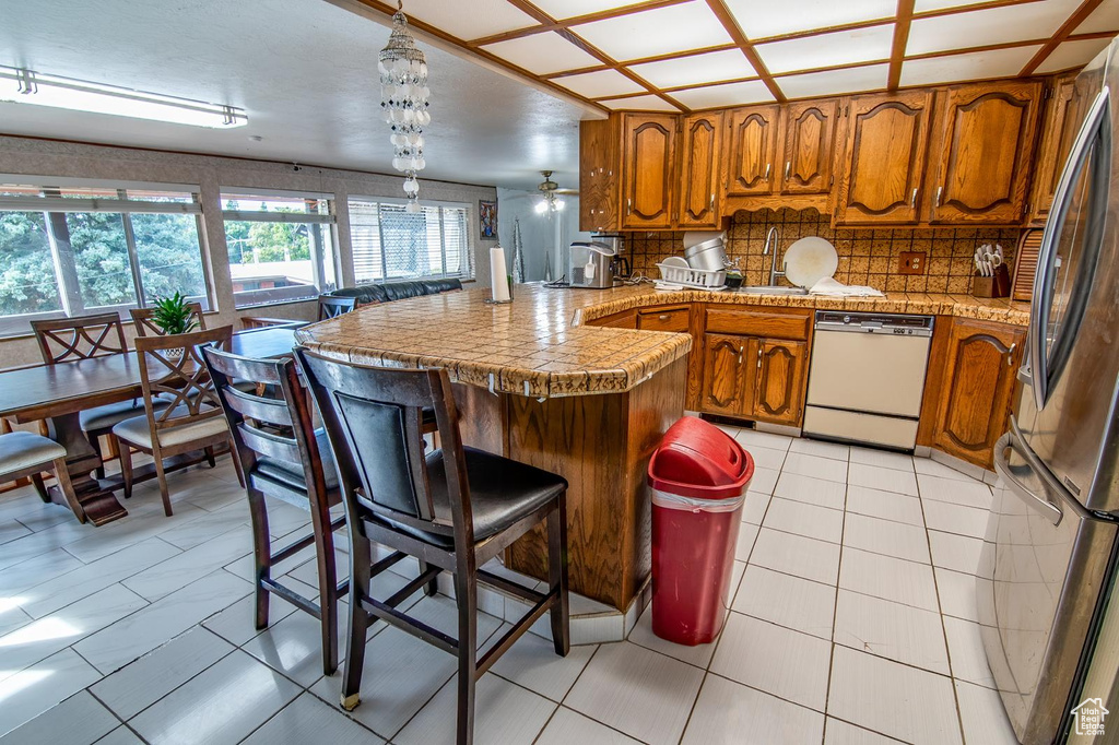 Kitchen with a peninsula, brown cabinetry, tasteful backsplash, freestanding refrigerator, and dishwasher
