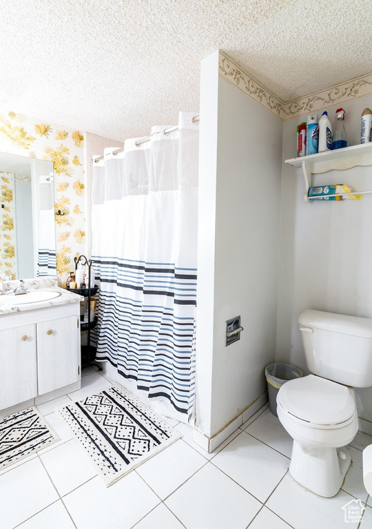 Full bath featuring toilet, tile patterned floors, wallpapered walls, and a textured ceiling