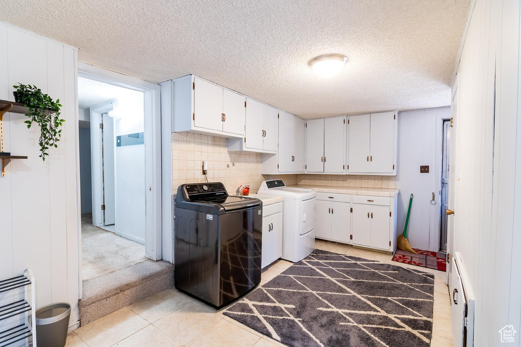 Laundry room featuring cabinet space, a baseboard heating unit, a textured ceiling, separate washer and dryer, and light tile patterned floors