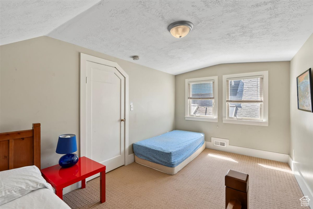 Carpeted bedroom with visible vents, a textured ceiling, baseboards, and vaulted ceiling