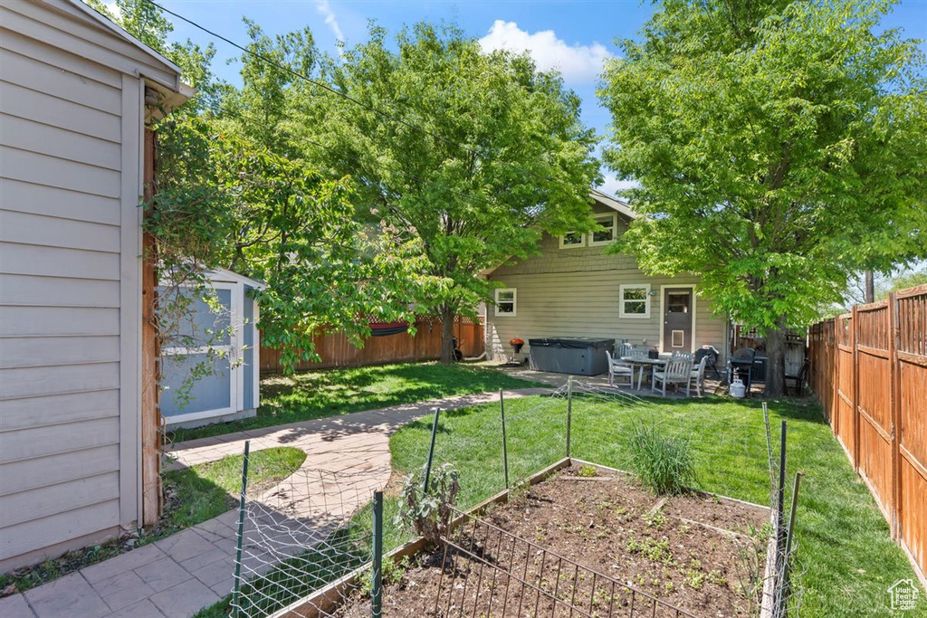 View of yard featuring a storage unit, a hot tub, a vegetable garden, a fenced backyard, and an outbuilding