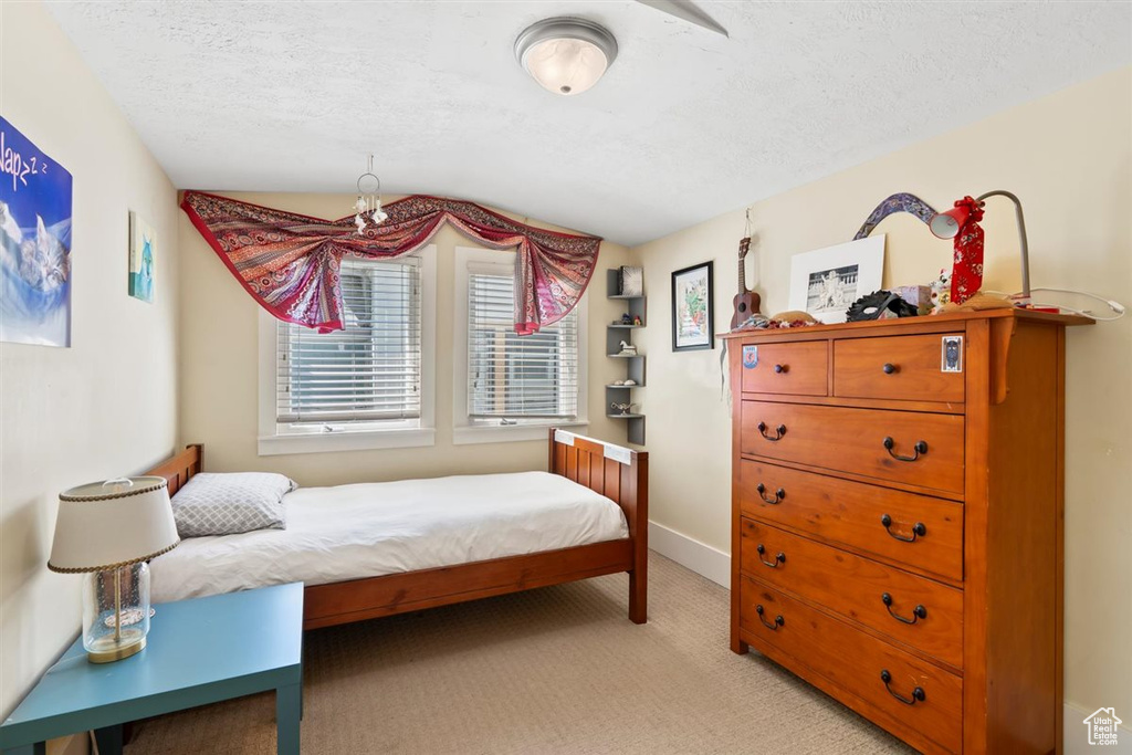 Bedroom featuring baseboards, light carpet, vaulted ceiling, and a textured ceiling
