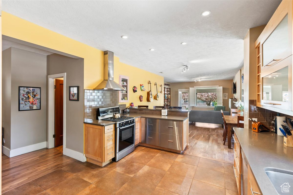 Kitchen with backsplash, range hood, a peninsula, open floor plan, and gas range oven